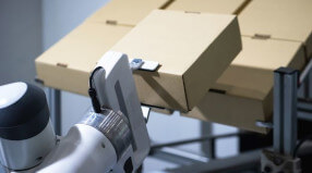 Robot arm handling cardboard boxes in a manufacturing setting